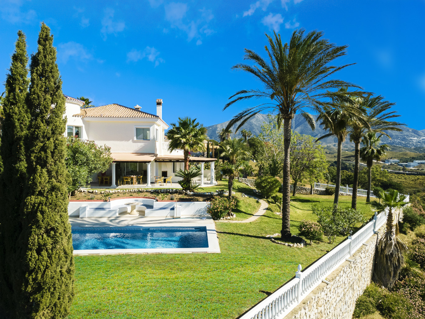 Weiße Villa mit Pool im Garten mit tropischen Pflanzen wie Palmen, sonniger Tag und blauer Himmel