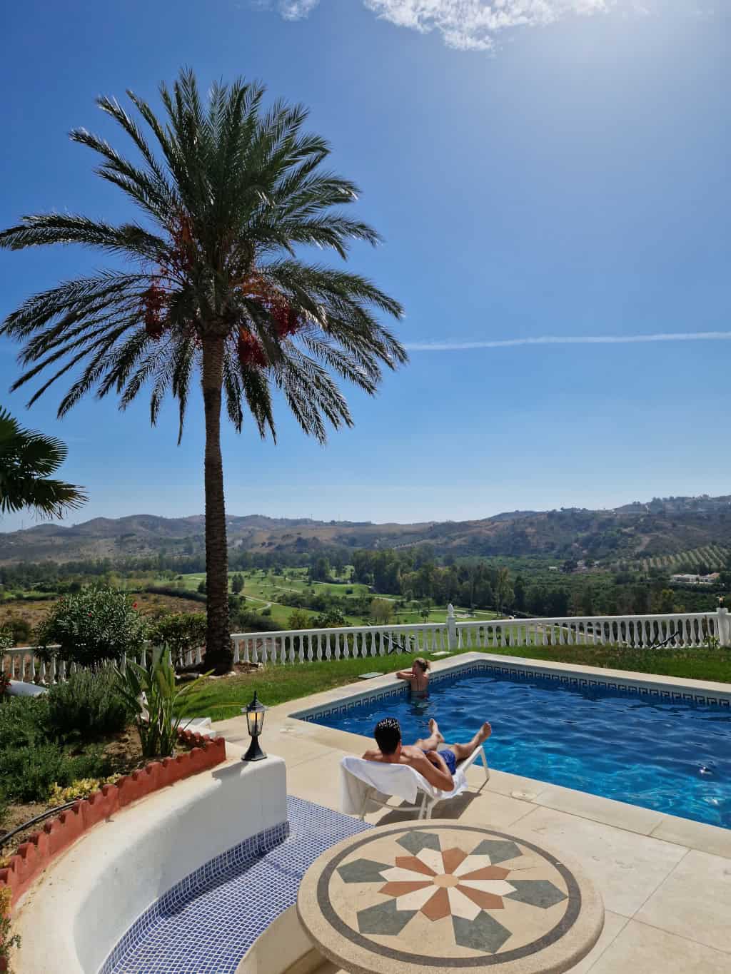 Pool picture with a guy on a sun lounger and a woman in the pool