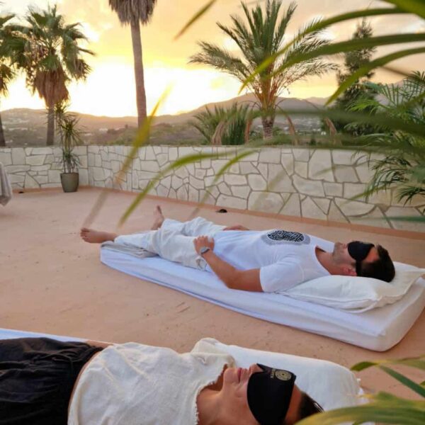 One guy and one woman laying on mattresses wearing blind fold, sunset in the background