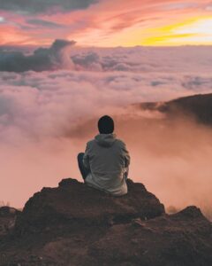 Guy meditating on cliff which is over the clouds during sun rise