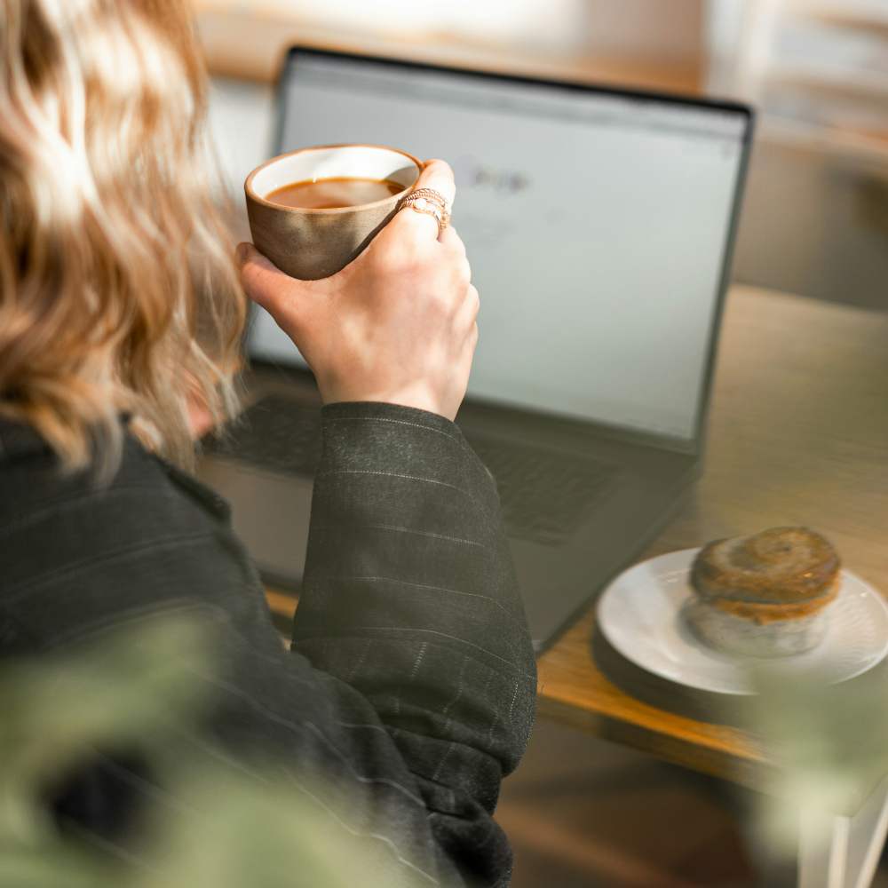 Woman holding cup of coffee in front of laptop