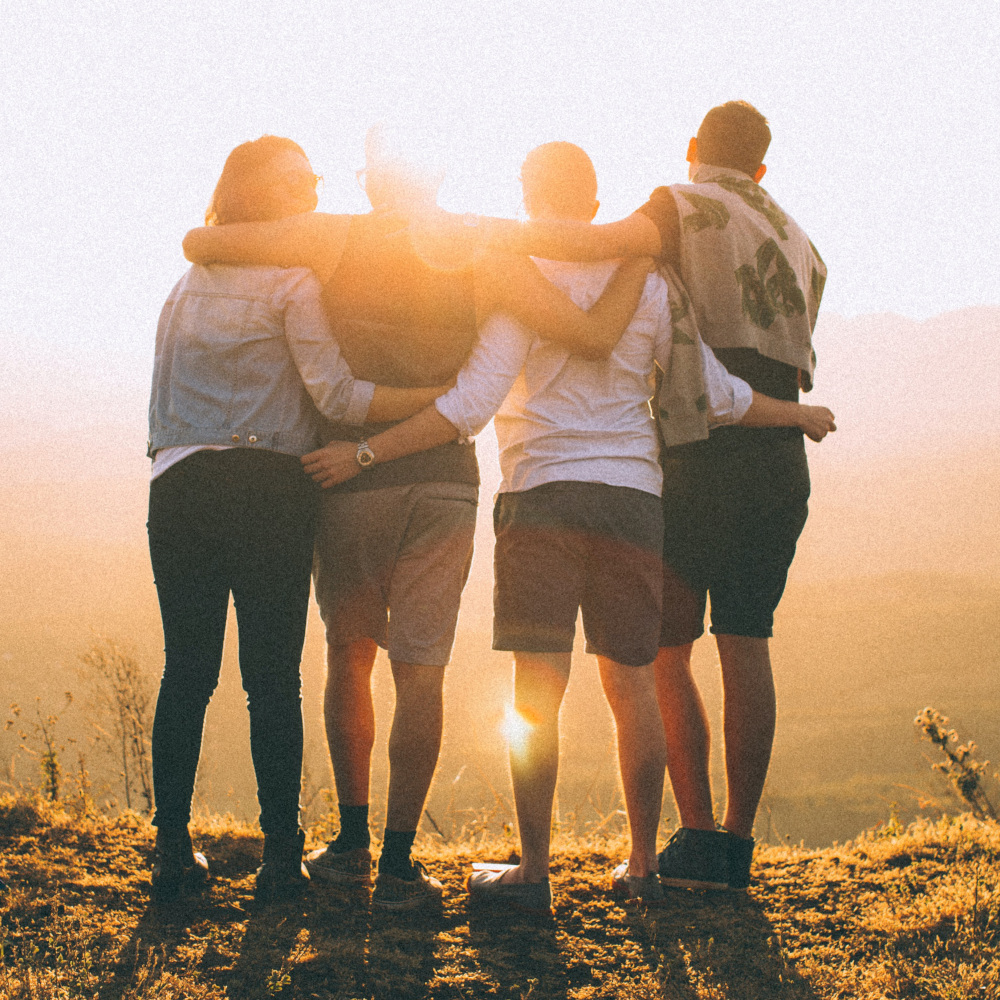 Four people holding each other in their arms during sun rise
