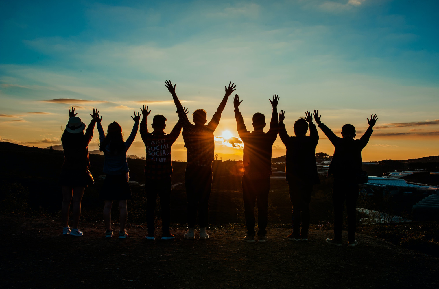 Group of 7 people raising hands towards sun rise