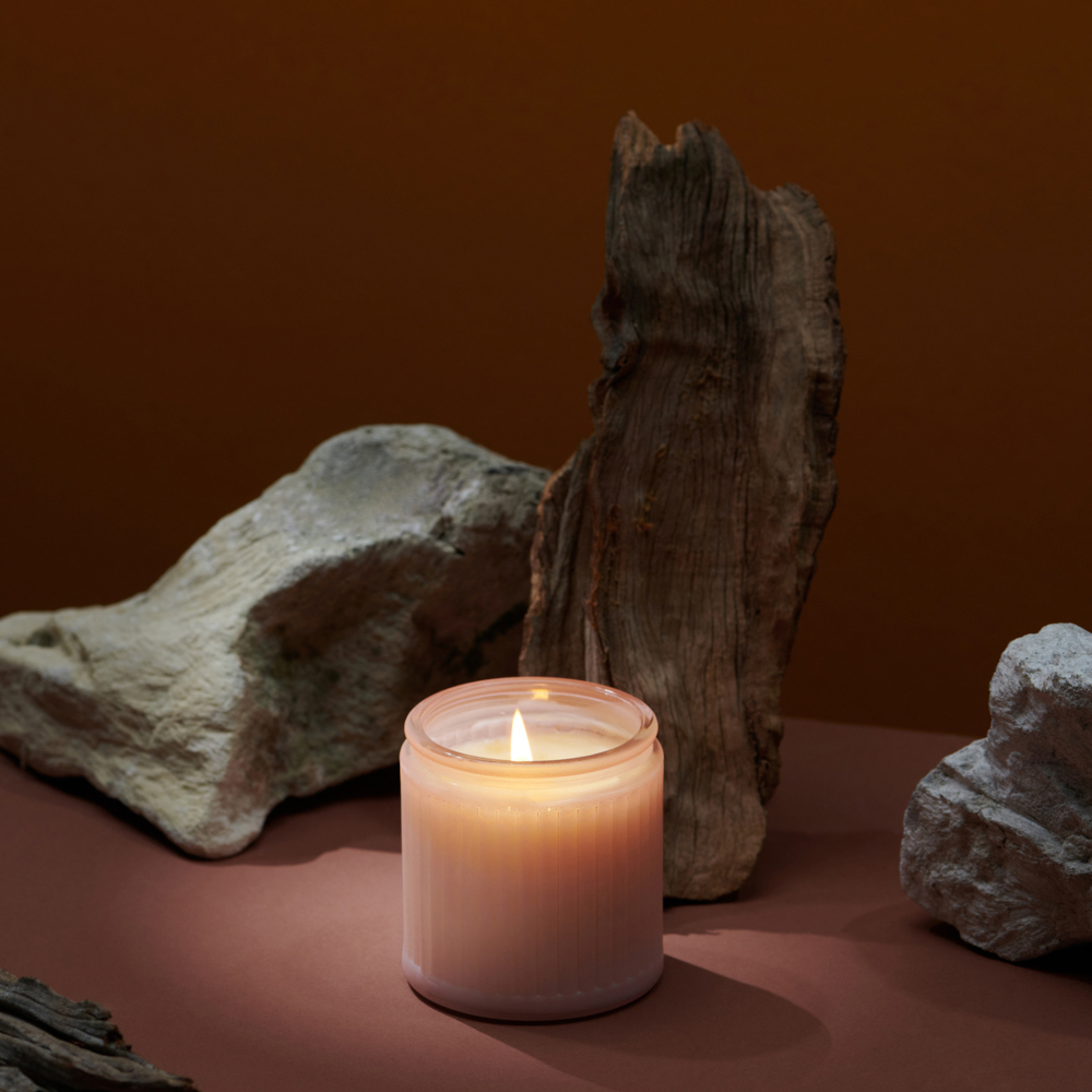Burning rose candle on rose background, bigger stones and wood next to the candle