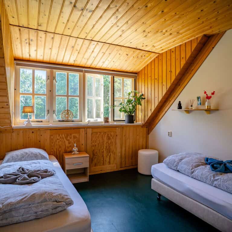 Bedroom with two separate single beds, sun shines through four windows