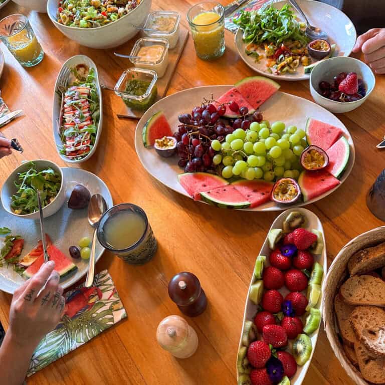 Food table with colourful fruits and people sitting around the table eating