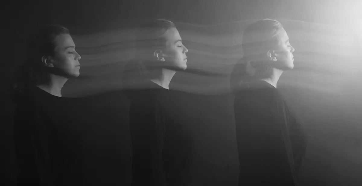 A black and white photo shows a woman in three overlapping positions, eyes closed, facing right. Blurred lines connect the figures, creating an effect of motion or transition. Light shines from the right side.