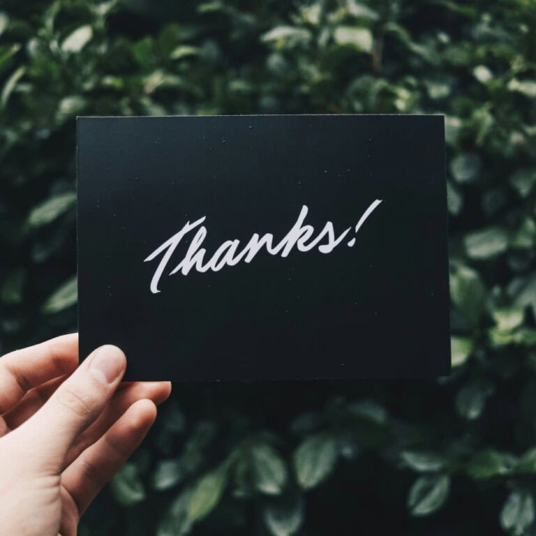 A hand holding a black voucher saying Thanks in front of green leaves