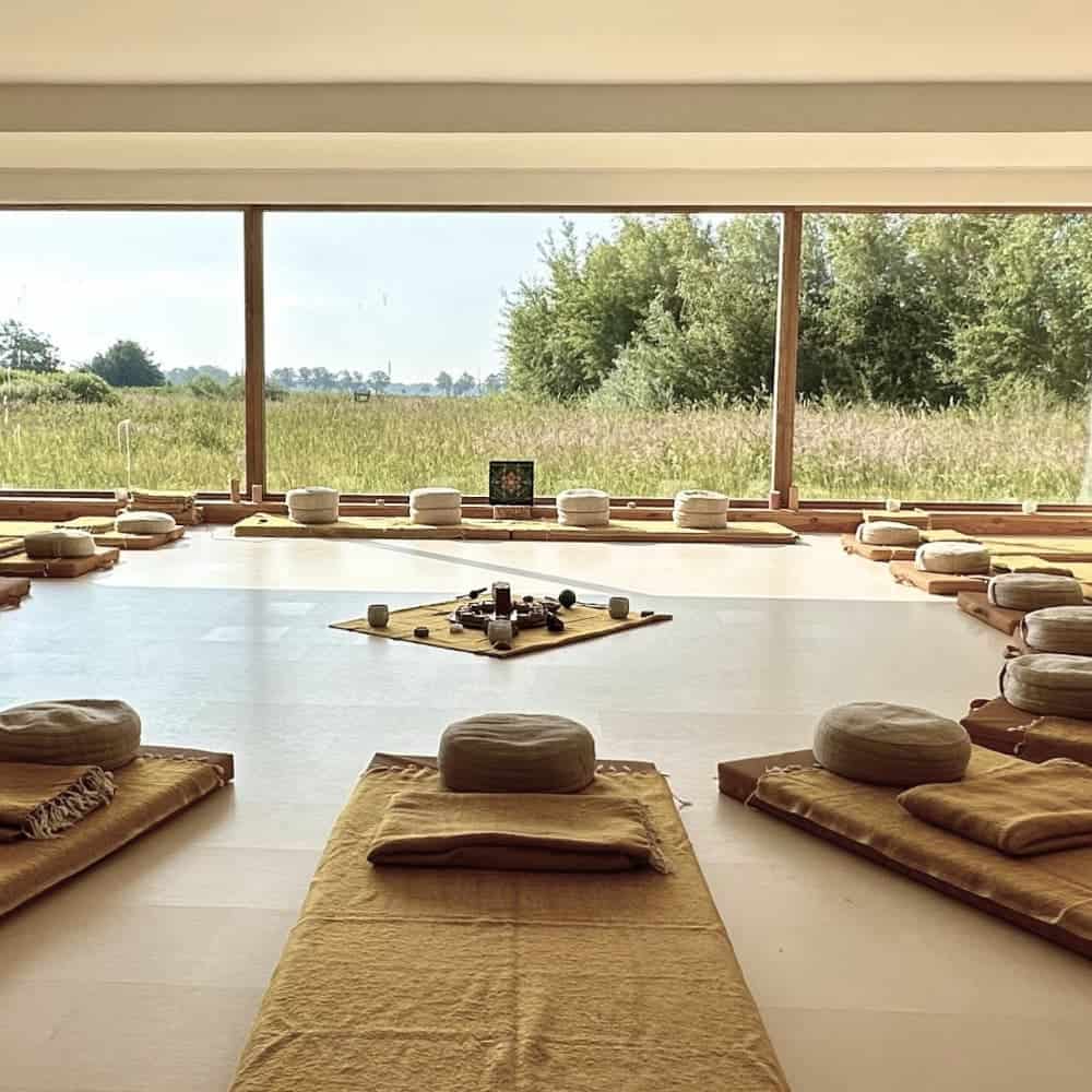 Interior of the large ceremony room at the retreat center. Through the large glass wall you have a view of the estate. Inside, the atmosphere is warm, and there are 12 mattresses with meditation cushions on them in a circle.