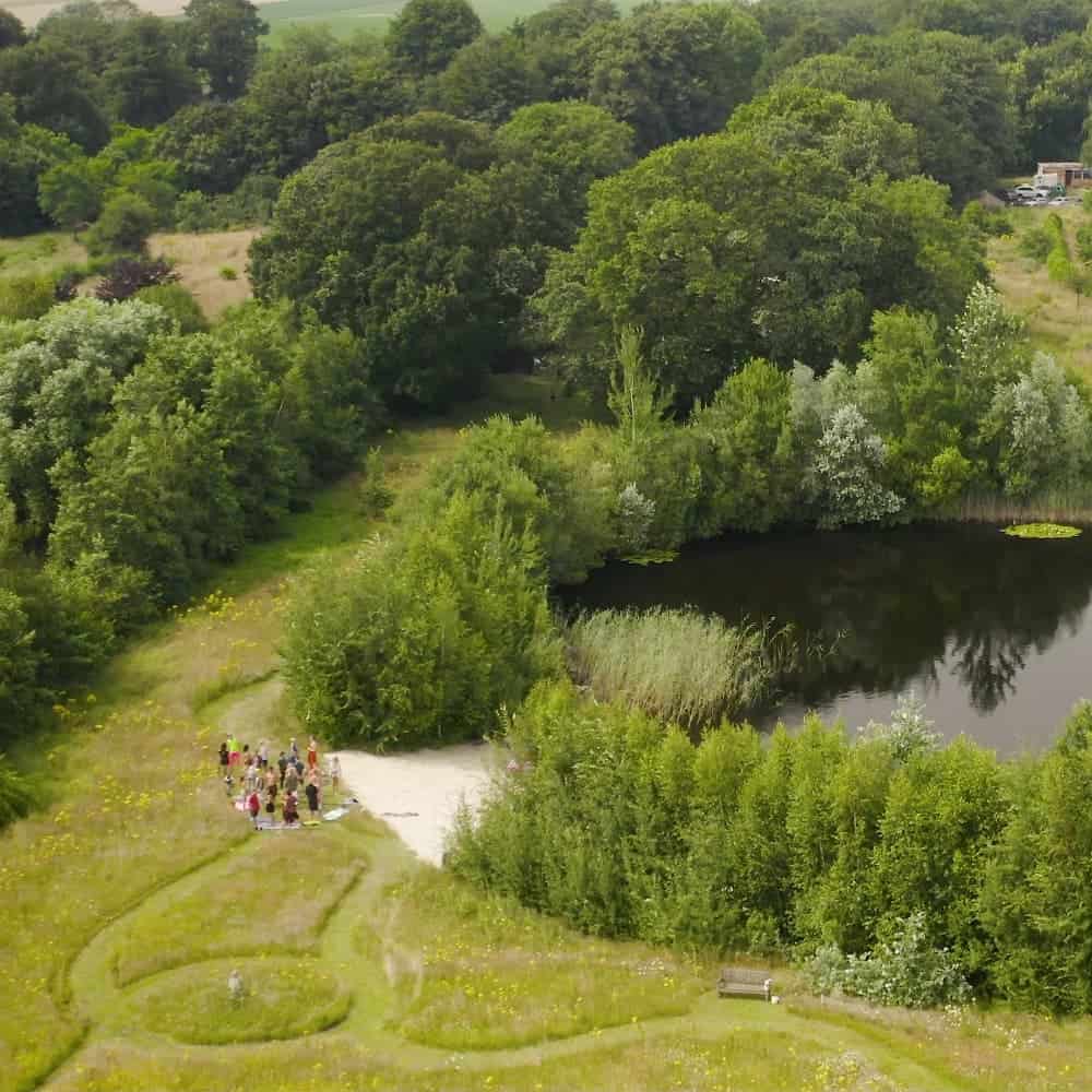 The swimming pond and private beach from birds-view. A large group of people stands by the private beach.