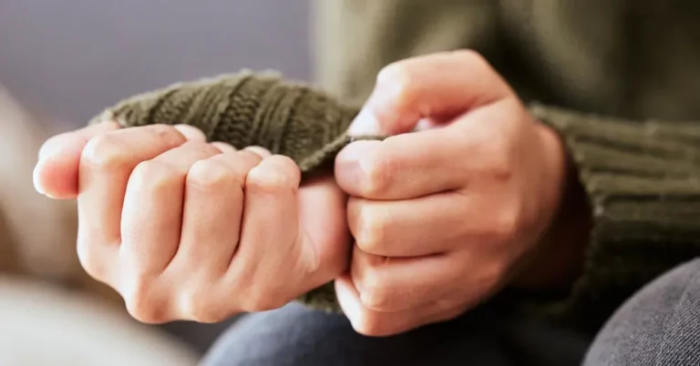 Close-up of a person pulling the sleeve of their green sweater over their fist, with both hands visible and fingers curled tightly, suggesting feelings of anxiety or nervousness.