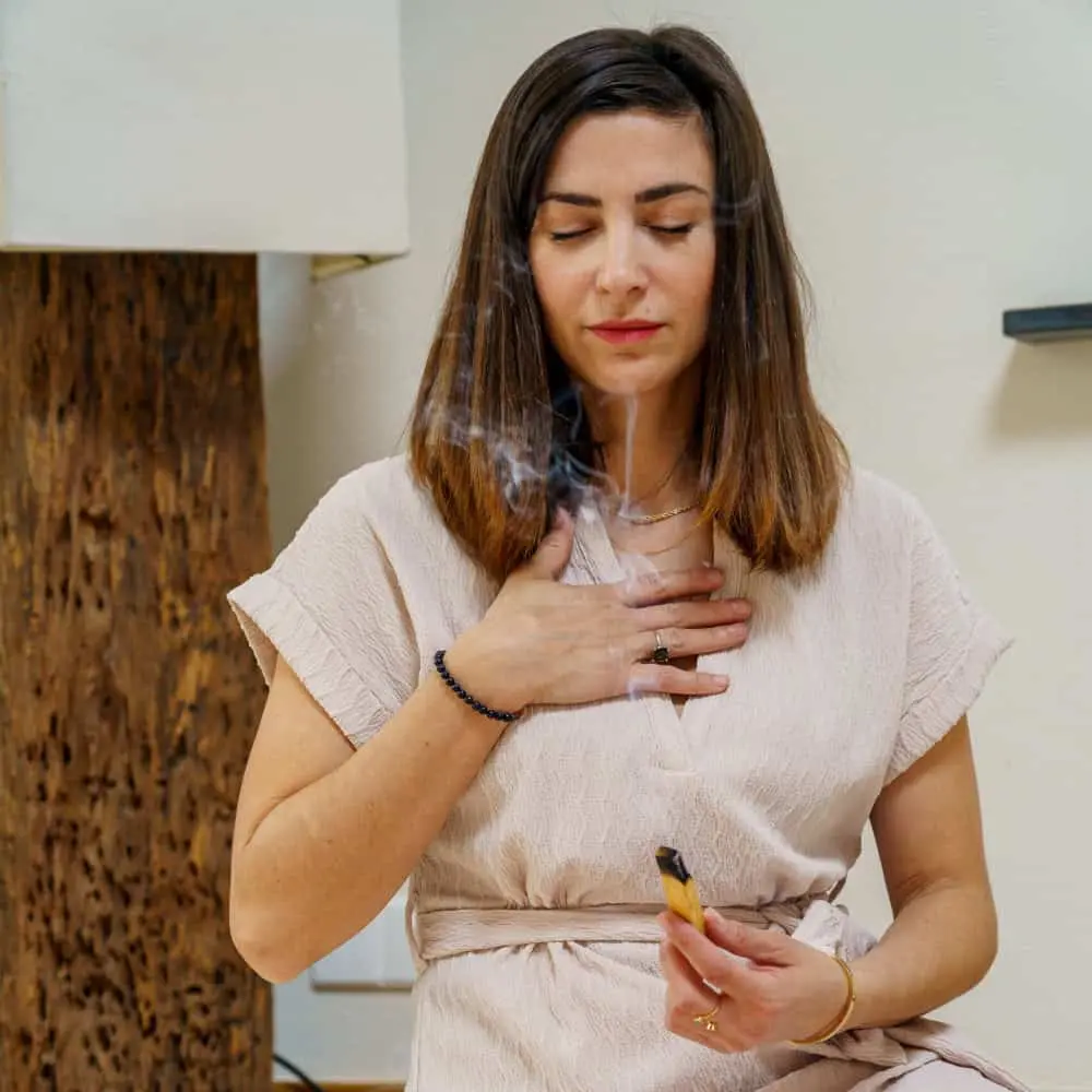 3-DAY Women Only Psilocybin Retreat Woman with brown hair, closed eyes holding a hand to her chest and using palo santo
